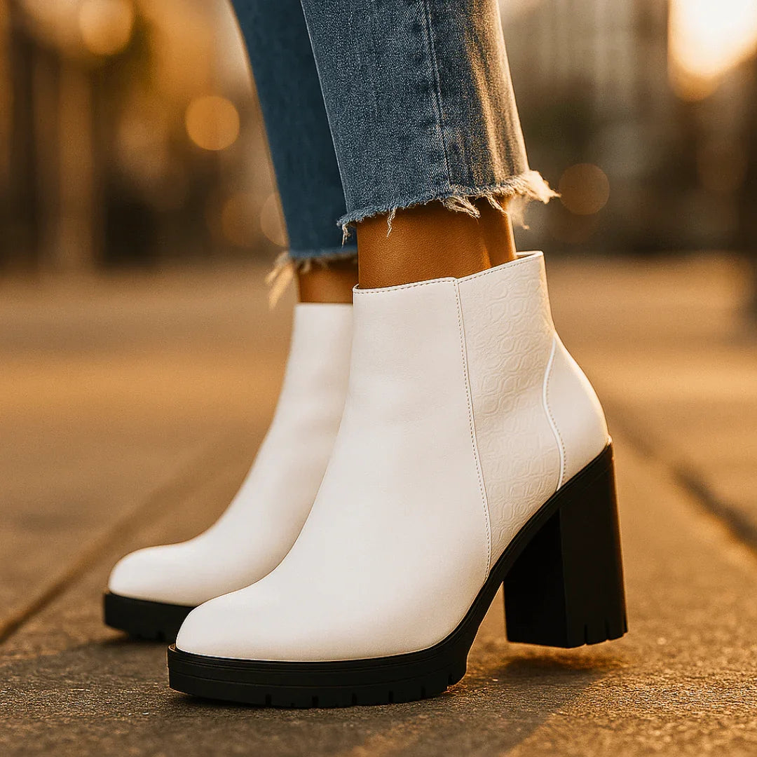 White ankle boots with black soles worn by a person on a blurred outdoor background