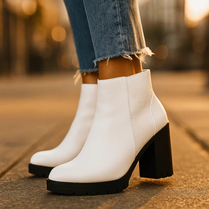 White ankle boots with black soles worn by a person on a blurred outdoor background